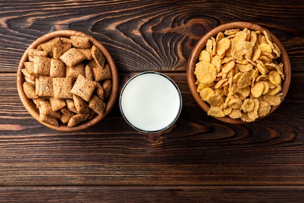 Corn flakes and dried chocolate pads on dark wooden table.