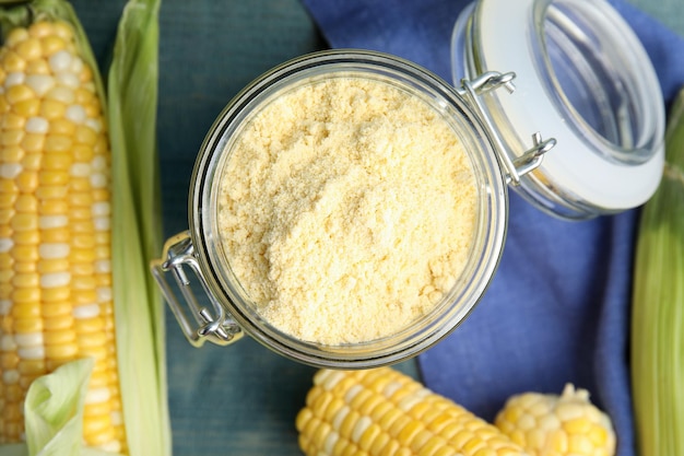 Corn flour in glass jar and fresh cobs on blue wooden table flat lay