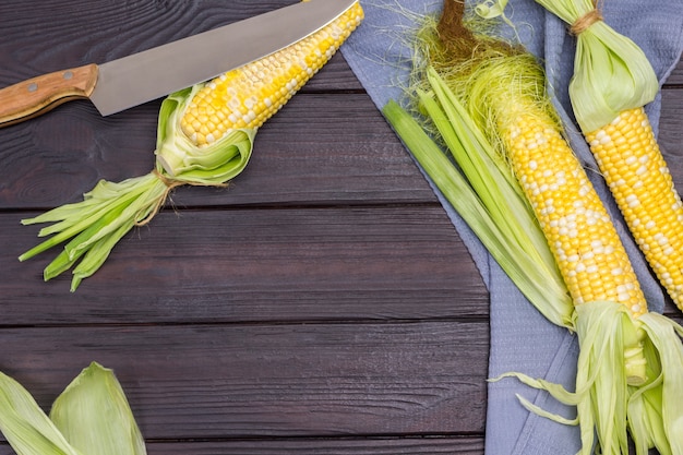 Corn on gray napkin Knife on corn Copy space Dark wooden background Flat lay