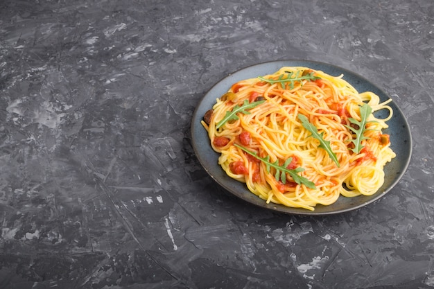 Corn noodles with tomato sauce and arugula on a black concrete background. Side view, copy space.