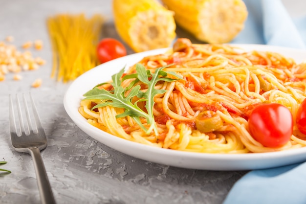 Corn noodles with tomato sauce and arugula on a gray concrete background. Side view, selective focus.