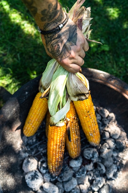 Corn ocobs roasted on coal grill man hand preparing food