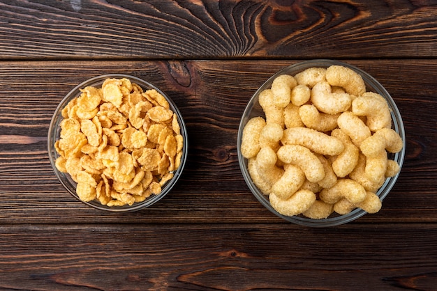 Corn sticks and corn flakes on dark wooden background.