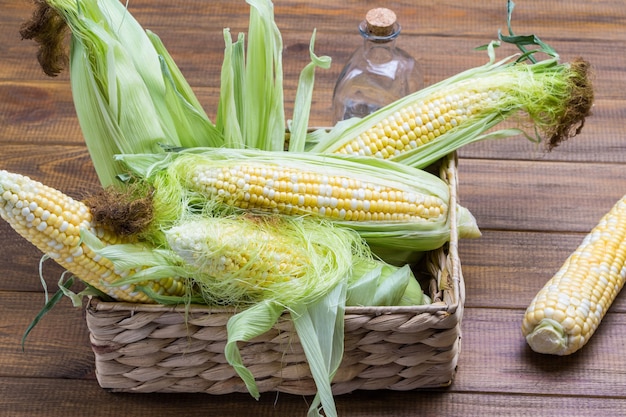 Corn with leaves in wicker basket Glass bottle Close up Wooden background