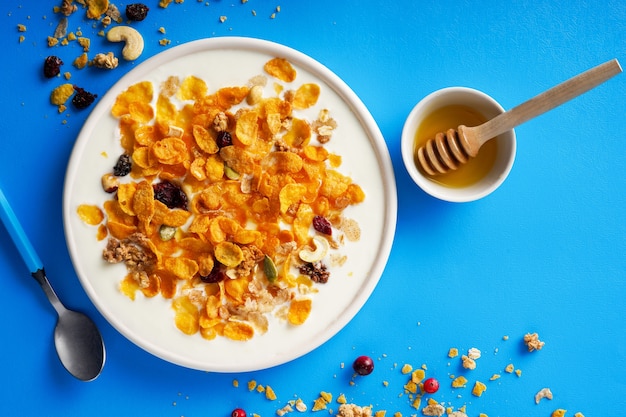 Cornflakes in a bowl with milk and honey on a bright blue background top view