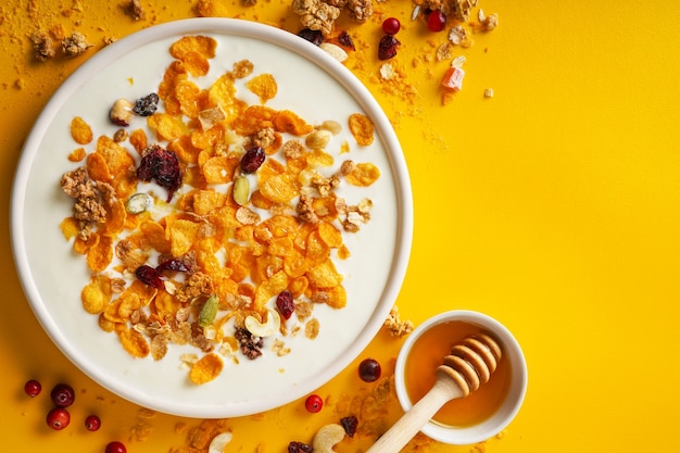 Cornflakes in a bowl with milk and honey on a bright yellow background top view