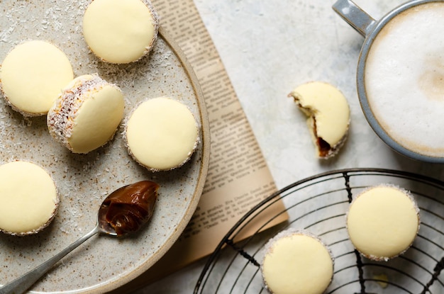 Cornstarch alfajores with milk caramel and coconut and a cup of latte on light grey background