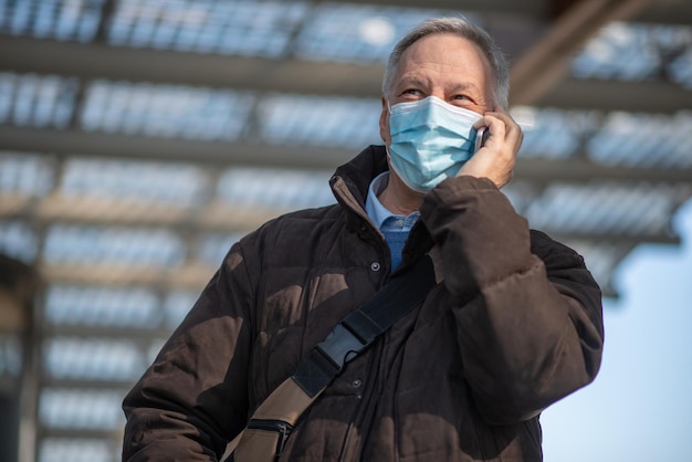 Coronavirus concept masked elder man talking on his smartphone outdoor