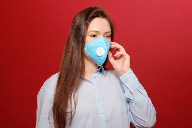 Coronavirus pandemic, close-up portrait of young woman on red background in protective medical mask,