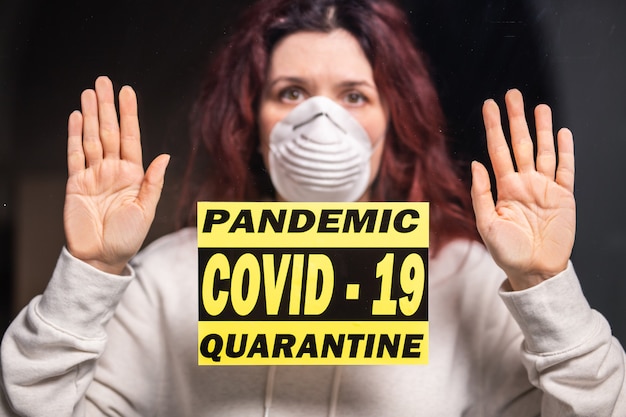 Coronavirus, quarantine, covid-19 and pandemic concept. Sad and sick woman of corona virus looking through the window