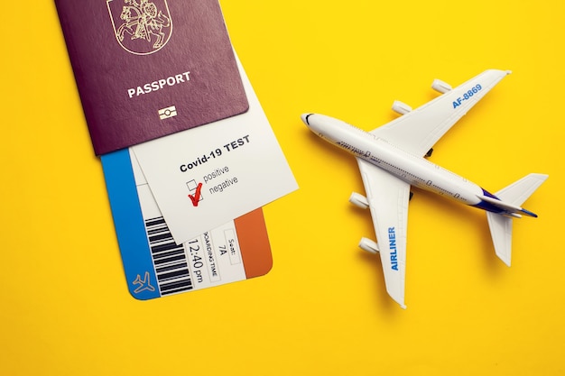 Coronavirus and safety travel concept, Covid-19 test with "Negative" mark, airline ticket, passport and plane on yellow background