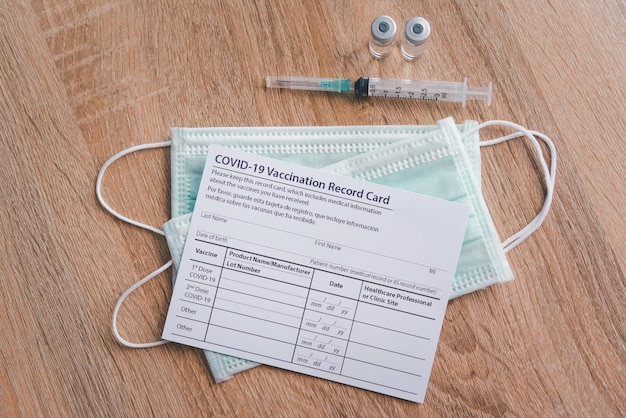 Coronavirus vaccination record card is placed on a wooden floor with a vaccine syringe