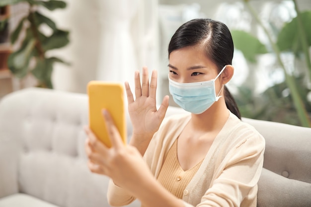 Coronavirus. Woman in quarantine for coronavirus wearing protective mask, she's working from home and using mobile phone at sofa