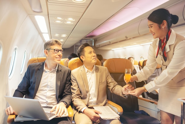 On a corporate aircraft an air hostess serves passengers On an airplane a flight attendant serves a drink to a businessman who is working on his laptop