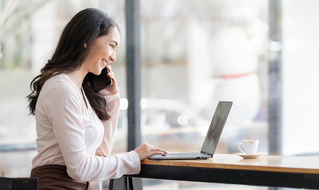 Corporate Communication Young Businesswoman Talking On Mobile Phone and Working On Laptop In coworkspace