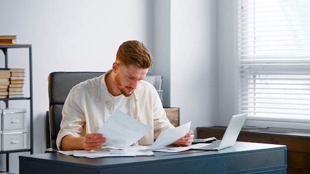 Corporate manager looks at sheets of papers with reports and analyzes company income