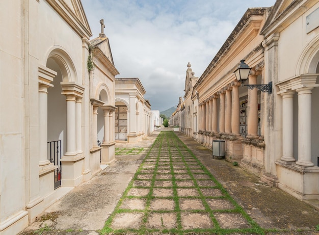 Corridor in a cemetery with tombs on the sides below cloudy sky