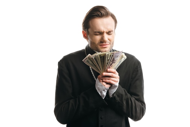 Corrupt catholic priest with closed eyes holding dollar banknotes isolated on white