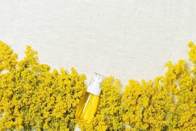 Cosmetic bottle container with yellow bedstraw herbs wildflowers on natural textile table