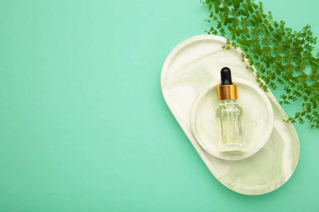 Cosmetic bottle of essential oil on plaster tray with green leaf on mint background