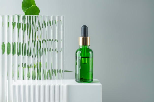 Cosmetic bottle serum oil on white stand with green branch on grey background Natural cosmetics concept skin care product Beauty concept for face body care Mockup