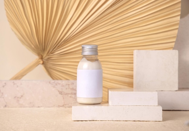 Cosmetic bottle with blank label on travertine stone against dry beige palm leaf close up mockup