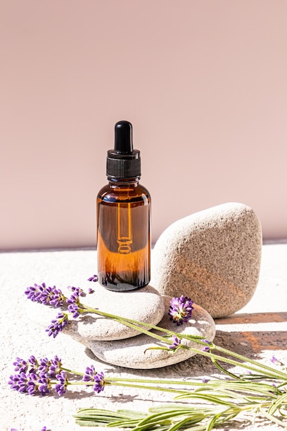 A cosmetic bottle with a dropper with a natural remedy based on lavender oil for facial skin care stands on natural gray stones packaging empty