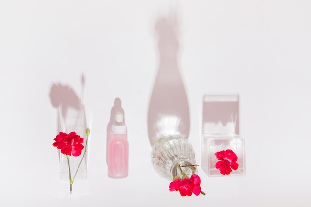 Cosmetic bottle with pipette and pink liquid Surrounded by pink flowers On a light background