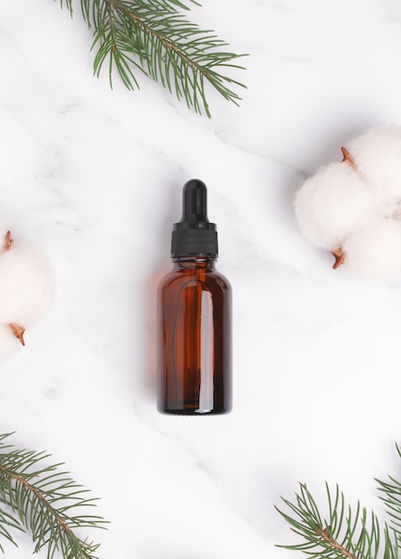 Cosmetic bottle with serum fir tree branch cotton flowers on marble background Hyaluronic acid oil serum with collagen and peptides Natural cosmetics