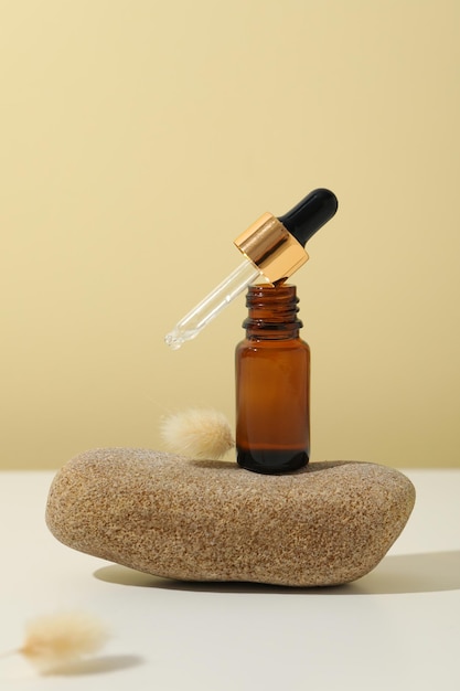 Cosmetic bottle with serum on stone on beige background