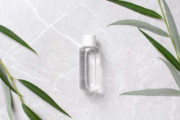 Cosmetic bottle with tonic water with leaves on marble background Hyaluronic acid oil serum with collagen and peptides skin care product Mockup packaging cosmetic design branding