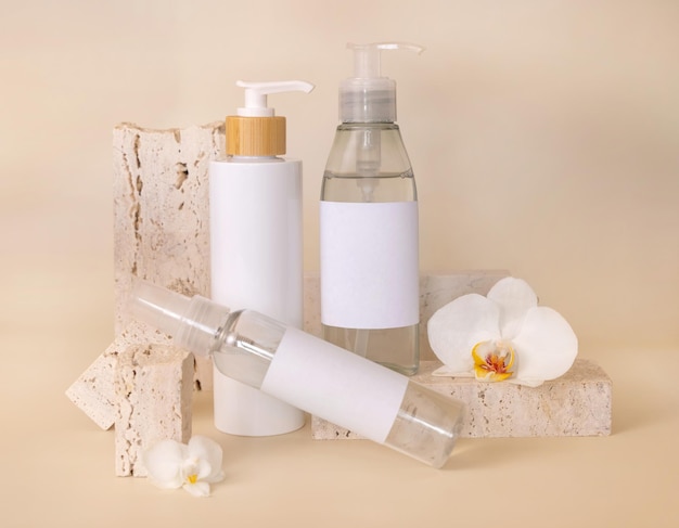 Cosmetic bottles near white orchid flowers and stones on light beige package Mockup