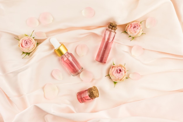 Cosmetic bubbles with rose oil and rose water on a pastel background made of textiles and rose buds. top view.