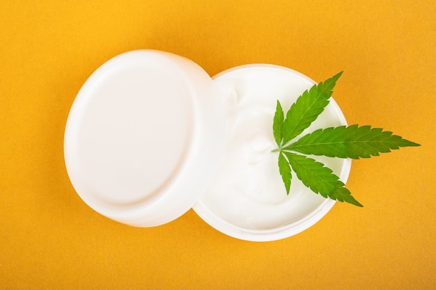 Cosmetic cream for combating wrinkles on the skin with cannabis on a yellow background.