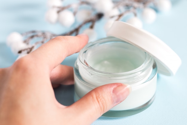 Cosmetic cream container on blue background with flowers. 