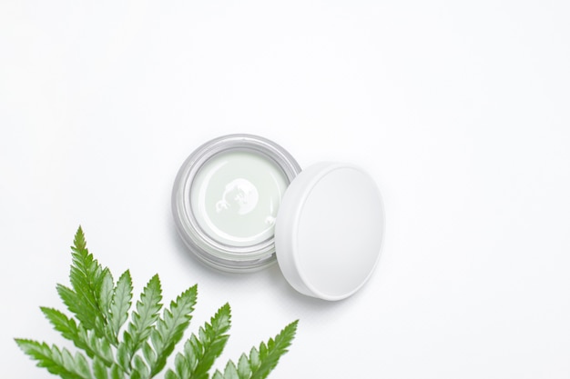 Cosmetic cream in container and fresh green leaves on white. Homemade spa, jar of organic cream, natural cosmetics, beauty products.