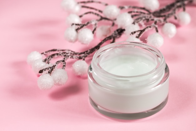 Cosmetic cream container on pink background with flowers. 