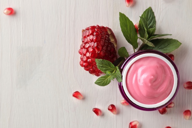 Cosmetic cream in a lilac jar and with fresh pomegranate on a white wooden table .