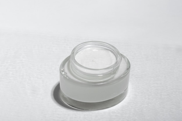 Cosmetic cream or mask in a glass jar with hard shadows from the leaves on a white background Natural organic care for face and body skin View from above