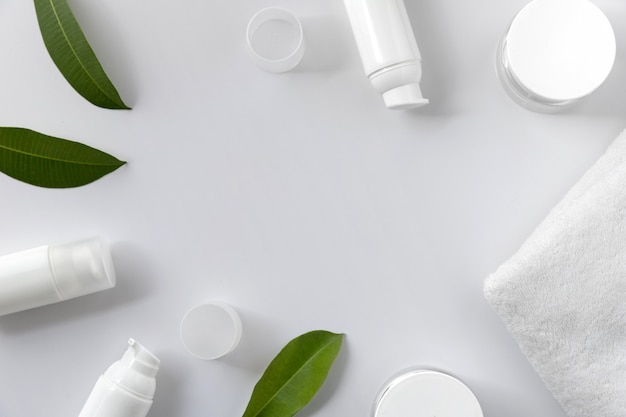 Cosmetic cream, towel and leaves on white background