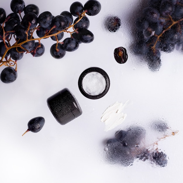 Cosmetic cream  with  black grapes around on wet trasnlucid background