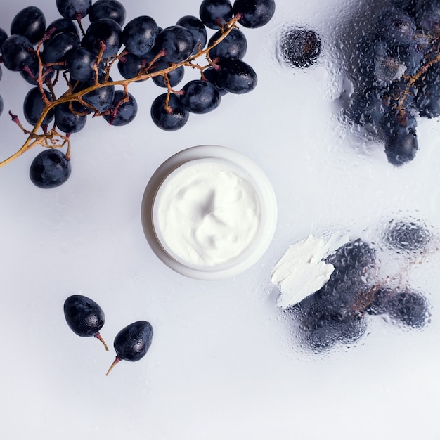 Cosmetic cream  with  black grapes around on wet trasnlucid background