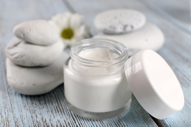 Cosmetic cream with spa stones and chamomile on wooden background