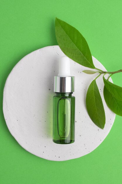 Cosmetic glass bottle with dropper and green leaves on podium The concept of a beauty salon and natural cosmetics