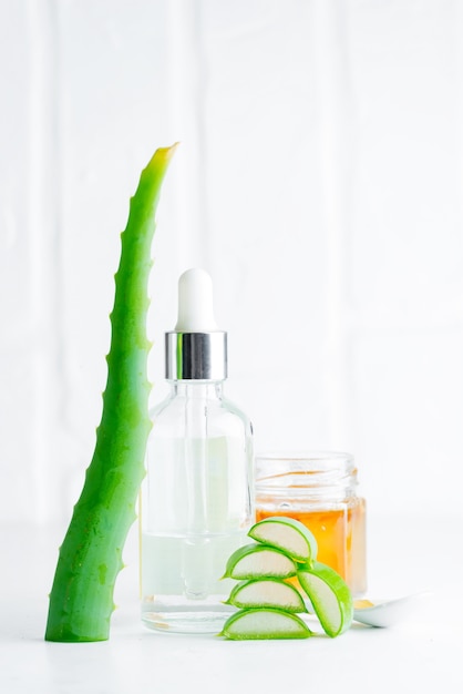 Cosmetic homemade lotion or essential oil from natural sliced aloe vera plant in glass bottles against light grey.