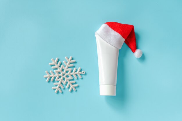 Cosmetic, medical white tube for cream, ointment or other product in red Santa Claus hat and white snowflake on blue 