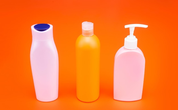 For cosmetic packing. Packaging bottles. Refillable bottles with flip cap and pump dispenser. HDPE orange background. Plastic liquid containers. Beauty products, copy space.