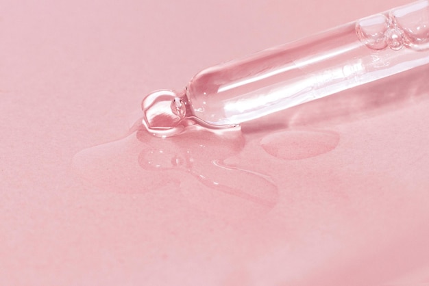 Cosmetic pipette with dripping liquid and drops on a pink background serum serum gel vitamin water oil