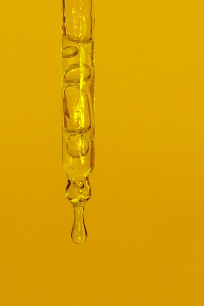 Cosmetic pipette with dripping liquid oil and drops on a yellow background serum serum gel vitamin water oil