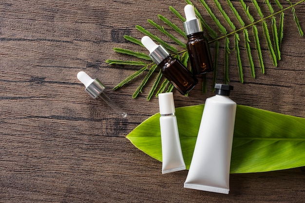 Photo cosmetic product and essential oil bottle on leaves over wooden table